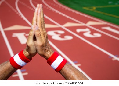 Hands Of Japanese Athlete Wearing Red And White Colored Wristbands Making Hopeful Prayer Gesture Of Gratitude Against A Red Athletic Track Background