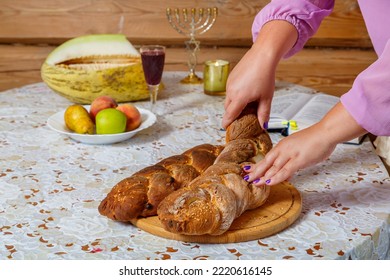 The Hands Of A Jewish Woman Break The Challah During The Shabbat Meal Next To Burning Candles And A Glass Of Wine. Horizontal Photo