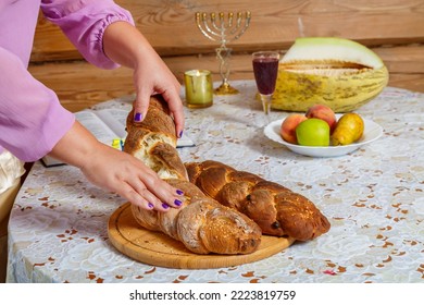 The Hands Of A Jewish Woman Break The Challah During The Shabbat Meal Next To Burning Candles And A Glass Of Wine. Horizontal Photo