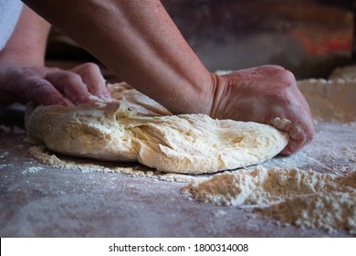 Hands kneading dough over a wooden bakery table with flour around