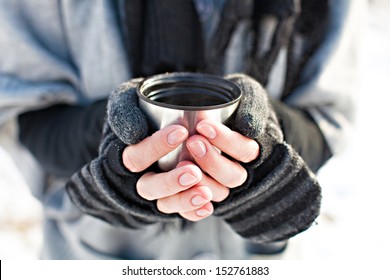 Hands in knitted mittens holding a cup of tea