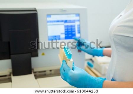 Hands of laboratory assistant loading sample tubes for coagulation test analysis and inputing data to coagulation machine.