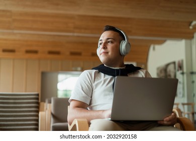 In The Hands Of A Laptop, Surf The Internet Online Training Using The Application. A College Student Listens To An Audiobook With Wireless Headphones.