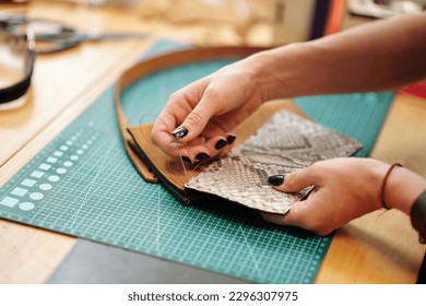 Hands of leather worker sewing parts of leather bag together - Powered by Shutterstock