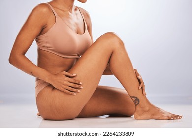 Hands, legs and skincare with a black woman in studio, sitting on the floor against a gray background for beauty. Fitness, body and tattoo with a female posing for hair removel, wax or laser