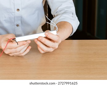 Hands lifting silver rectangular device with attached multicolored wires from desk surface