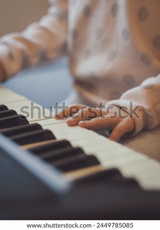 The hands of a little caucasian girl presses the keys on an electric piano while sitting on a sofa in the room, close-up side view with depth of field. Music education concept.