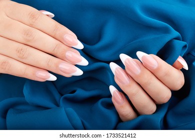 Hands and long artificial french manicured nails blue textile background