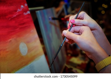 Hands Of Loving Couple Holding Paint Brush, Touching And Creating A Nice Picture Of Sunset. Man And Woman Paint Their Picture Of Sunset On The Seashore. Art Workshop. Make A Date To Draw A Picture