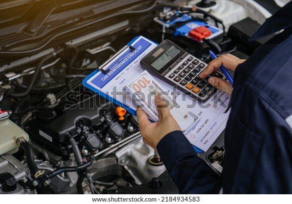 Hands\
of machinic man holding calculator and money, dollar banknotes to\
charge service and writing to the clipboard the checklist for\
repair machine.Services car engine machine\
concept.