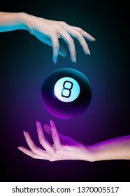 Hands with magic billiard ball number eight on a dark background. Cyan and purple light