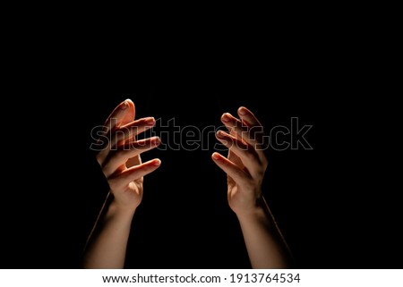 Hands make magic, or pray that the light falls from above on hand. Radiance between the palms. Gestures, black background