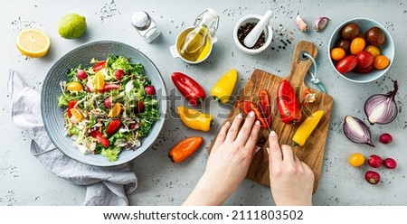 Cook’s hands making fresh colorful spring vegetable salad with cherry tomatoes and peppers in the blue bowl. Healthy organic vegan lunch. Kitchen worktop captured from above (top view, flat lay).