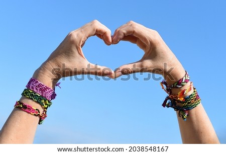 Hands making heart symbol on sky background. friendship bracelets on wrists