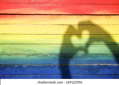 Hands making love heart shadow symbol of tolerance on gay pride rainbow colors painted on slats of weathered wood