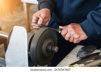 hands of a male artisan sharpener grinder sharpening knife blade on a sharpening machine close-up - Powered by Shutterstock