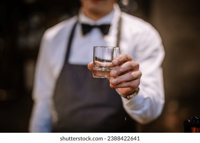 hands of a male bartender accurate holding clean transparent empty glass for booze. Blurred bar background