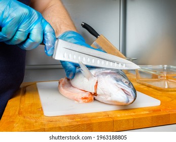 The Hands Of A Male Cook In Hygienic Gloves Cut Off The Head Of A Salmon With A Knife. Cutting Fresh Fish In The Kitchen On A Cutting Board.