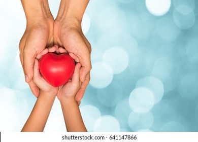 Hands of male dad and little child girl holding red heart ball together with blur green natural light bokeh background. Happy father's day father and daughter concept.  
