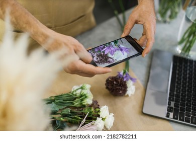 Hands Of Male Florist Holding Smartphone Taking Picture Of Flower On Counter. Flat Lay, Top View Mockup. Floristics, Business, Decoration Concept. Close Up.