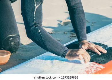 Hands of male surfer in wetsuit waxing surfboard on sand on ocean beach. Cropped shot. Surfing and active lifestyle concept - Powered by Shutterstock