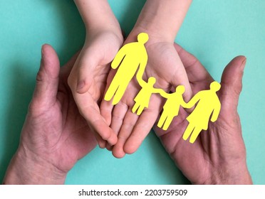 The Hands Of A Man And A Child Hold A Silhouette Of A Family With Children Cut Out Of Yellow Paper. The Concept Of Family Traditions And Values, Succession Of Generations. Family With Small Children