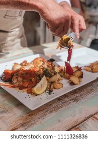 Hands Of Man, Cook, Delivering Cooked Fish, On The Plates Of The Diners. Typical Food Of Ibiza, Spain.