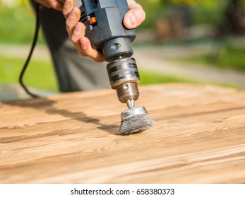 Hands man with electrical rotating brush metal disk sanding a piece of wood. Woodworking outdoors.
