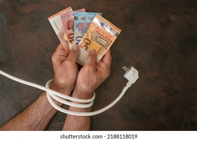 Hands of a man with euro banknotes and are tied up with an electric power cable, concept for rising electricity costs and saving energy, dark background, copy space, top view, selected focus - Powered by Shutterstock