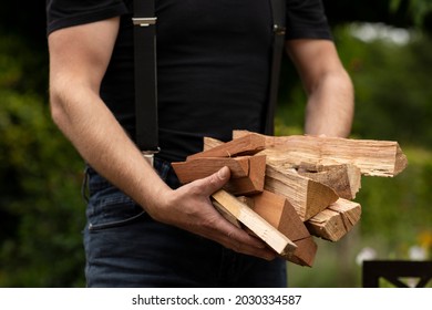 Hands Of A Man Holding Logs Of Fire Wood To Use For Heat And Warmth In His Outside Stove Surrounded By Greenery. Lumberjack Gathering And Preparing Wood Pieces For His Alternative Heating