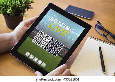 hands of a man holding a online betting device over a wooden workspace table. All screen graphics are made up.