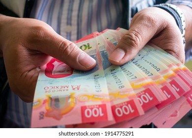 Hands of a man, holding a pile of mexican 100 bills, 