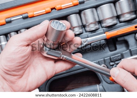 Hands of a man holding a ratchet wrench in the background you can see the toolbox.