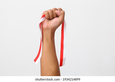 The Hands Of A Man Holding A Red And White Ribbon As A Symbol Of The Indonesian Flag. Isolated On Gray Background