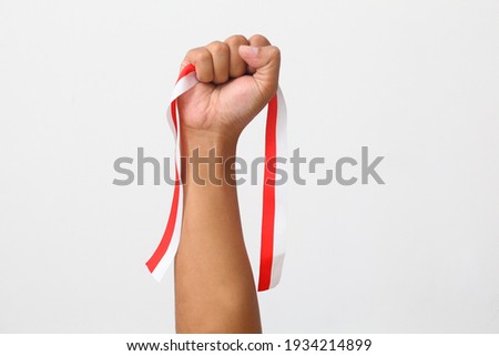 The hands of a man holding a red and white ribbon as a symbol of the Indonesian flag. Isolated on gray background
