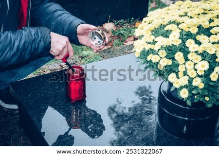 hands of man lighting candles on graves decorated with lanterns, burning candles, colorful chrysanthemum flowers, catholic symbols