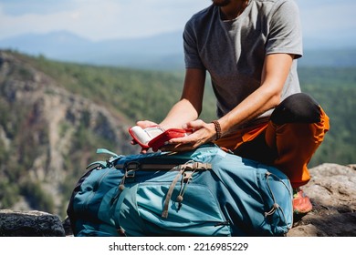 The Hands Of A Man Opened The First Aid Kit On A Hike, The Hand Holds An Open Bag With Medicines, A Hiking Set Of Equipment, A Man In The Mountains. High Quality Photo