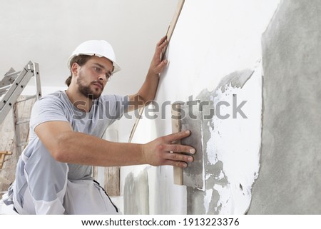 Hands man plasterer construction worker at work with trowel, plastering a wall, closeup