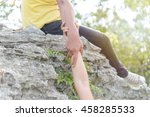 The hands of a man pulling a woman"s hands up the cliff  with bright sunlight
