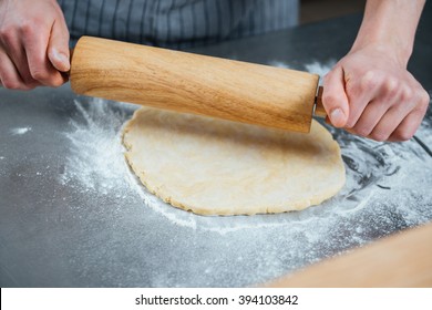 Hands Of Man Rolling Out Dough Using Rolling Pin On The Table