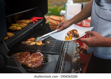 Hands Of Man Serving King Prawns From An Outdoor Barbecue Grill That Also Grills Other Meats And Vegetables.