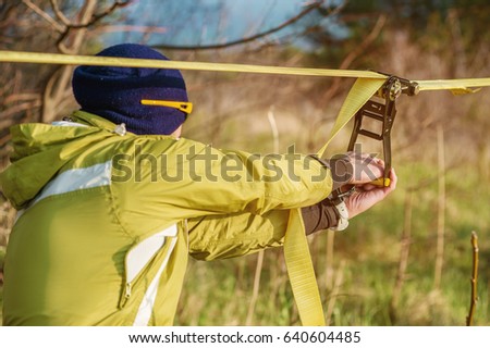 Hands of A man sets up slacklining equipment before doing crazy slacklining tricks and walking on slacklin in a park in the nature