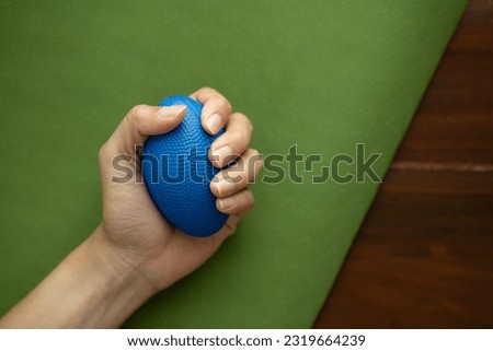 Hands of a man squeezing a blue stress ball on the yoga mat