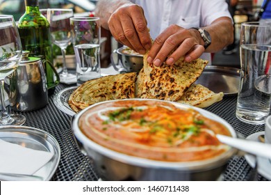 Hands Of Man Tearing Bread (butter Naan) At The Table With Indian Meals, Glasses Of Water And Wine, Jug With Tea, Outdoor In Indian Restaurant.