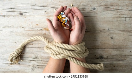 Hands of man are tied with a rope and in his hands he holds many different pills, concept addiction, drug addiction, photo taken from above - Shutterstock ID 1951133980