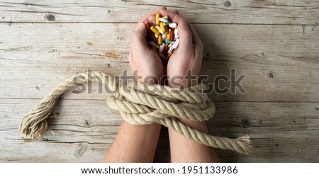 Hands of man are tied with a rope and in his hands he holds many different pills, concept addiction, drug addiction, photo taken from above