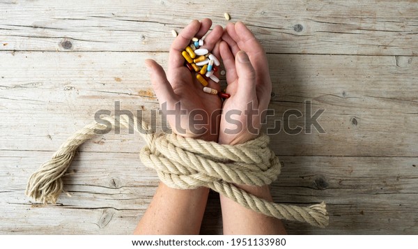 Hands of man are tied with a rope and in his\
hands he holds many different pills, concept addiction, drug\
addiction, photo taken from\
above