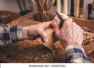 Hands of a man using a knife to carve a small piece of wood on a workbench - Powered by Shutterstock