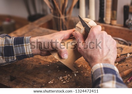 Hands of a man using a knife to carve a small piece of wood on a workbench