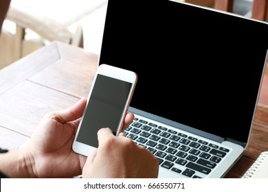 Hands of man using mobile phone while having laptop